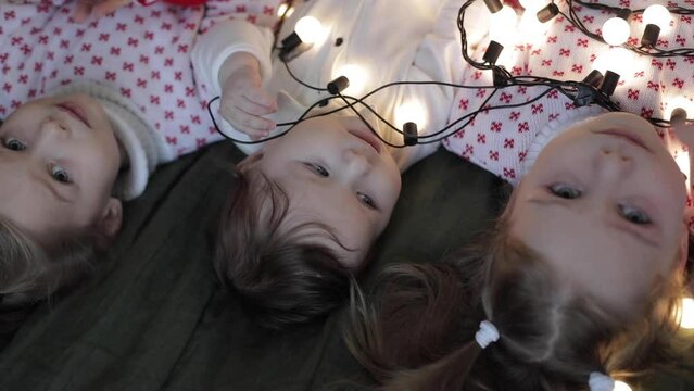 little cauacsian boy lies with his elder sisters under a lot of lights