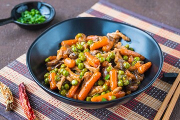 Asian style pork with mini carrots and green peas in a ceramic bowl on a brown concrete background. Wok dishes.
