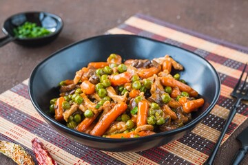 Asian style pork with mini carrots and green peas in a ceramic bowl on a brown concrete background. Wok dishes.