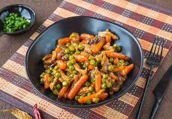 Asian style pork with mini carrots and green peas in a ceramic bowl on a brown concrete background. Wok dishes.