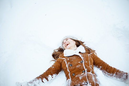 smiling stylish woman in sheepskin coat making snow angels