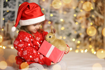  Christmas card with a baby and a rabbit in a box. Child is happy with a New Year's gift. The background is defocused light. Concept of Christmas and New Year. High quality photo