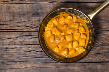 Chicken in curry cream sauce in a frying pan on a dark wooden background
