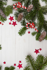 Fototapeta na wymiar Green Christmas tree branches with pinecones decorated with red stars and Christmas candy canes on a white wooden background top view