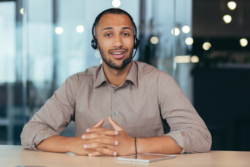 Portrait of a young handsome African American man. He sits in a headset in front of the camera, talks, consults. Business training, webinar, customer support service, online store.