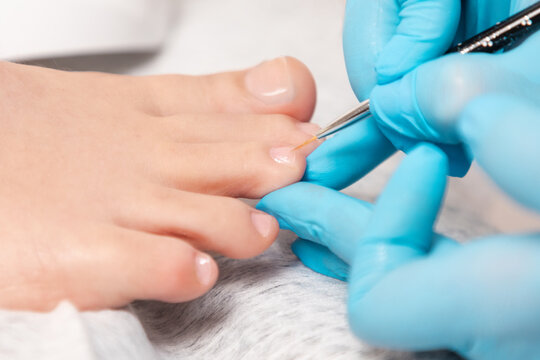 A pedicure master in medical gloves takes care of beautiful female toenails. Close-up. The concept of chiropody and podology