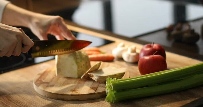 Cropped female housewife hands chopping, cutting turnip with diligence using kitchen knife on wooden board. Cook hobby