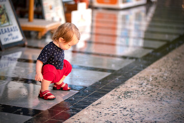 Small child walks on a rainy day. Toddler walks on a wet road in red sandals. Looks into the reflection