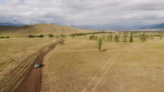 Flying over a valley over an SUV driving on the road towards high mountains on a sunny summer day. tourist trips to the mountains. Drone video