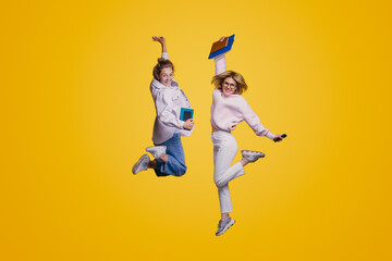 Full length portrait of a two overjoyed teenage students jumping isolated over yellow background....