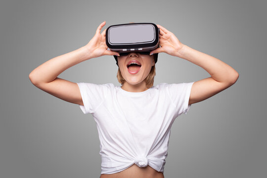 Front view of a woman wearing vr goggles headset watching on gray background. Metaverse concept. Future computer technology. Futuristic lifestyle.
