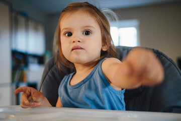 Baby sitting on a high-chair eating while pointing at the camera. Great design for any purposes....