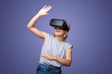Woman in modern VR glasses having virtual reality experience isolated over purple background. Augmented reality game, future technology. Futuristic lifestyle.