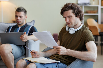 Portrait of two roommates living together, focus on young man studying or preparing for exams in foreground