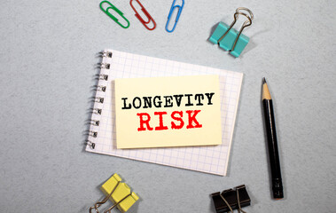 On the office table there is a calculator, a notebook with the text LONGEVITY RISK, a pen, glasses and dollars.