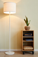 Minimal background image of floor lamp with cozy yellow light against beige wall with decor elements