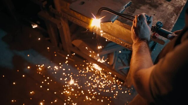 A steel industry worker cuts a piece of metal using a gas welding torch