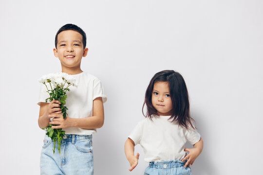 pleasant, happy brother and sister of preschool age stand on a light background and the boy holds a bouquet of daisies in his hands. Themes of relationships and friendship between children