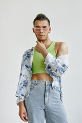 Vertical portrait of young gay man wearing extravagant outfit with crop top against white in...