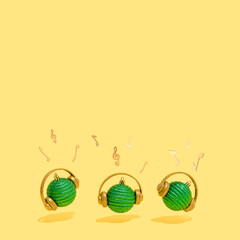 Three green Christmas decorations with headphones and musical notes on a yellow background. Concept of Christmas, New Year and winter holidays party, music and happiness. Good Vibes.