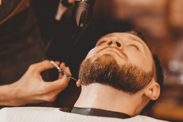 Barbershop concept vintage toning. Barber shearing beard to man in hair salon