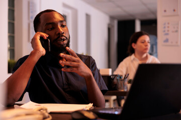 Project manager discussing startup strategy with colleague on smartphone, employee answering coworker mobile call. Businessman having telephone conversation in coworking space at night