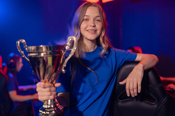 Young woman holding cup trophy prize of victors video games tournament esport, neon color, soft focus. Professional gamer of team computer players