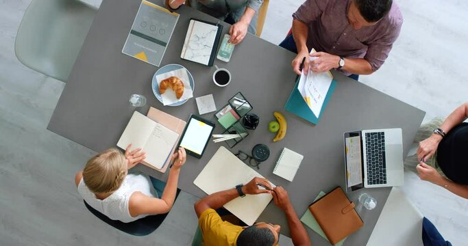 Meeting, planning and collaboration with a team sitting around a table from above with technology. Laptop, documents and diversity with a business woman writing in an office with man colleagues