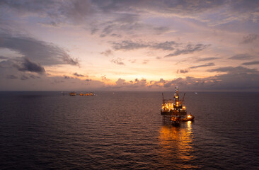Jack up drilling rig and production platform in the middle of the ocean at sunrise time.