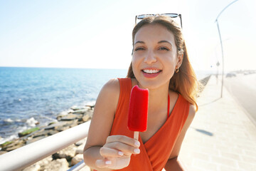 Funny Brazilian girl eating popsicle on promenade. Summer vacation concept.