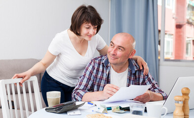 Husband and wife with financial documents near laptop