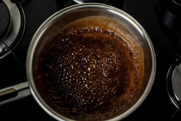 Chocolate icing boiling in pan on stove.