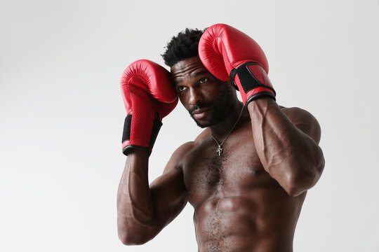 Athletic young man with naked torso and good physique boxing with red gloves. 