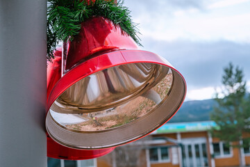 Two large christmas red bells with red bow and pine leaves, street Christmas decoration, left side close up view, blurry background