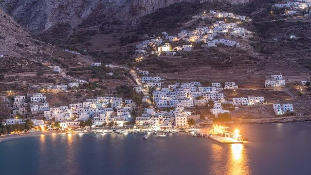 Amorgos island aerial day to night transition timelapse from above after sunset. Traditional Greece - illuminated white houses on hills and turquoise sea, Cyclades