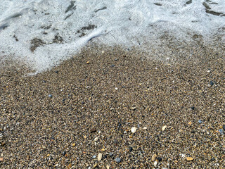 Waves of water in the sea and sand with small natural multi-colored stones on the seashore, small pebbles on the beach. Background, texture