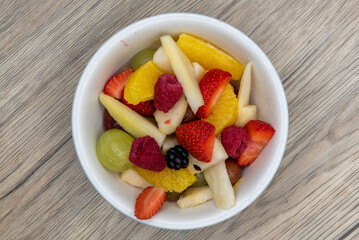 Overhead view of generous bowl of fresh sliced fruit including strawberry, pear, and orange