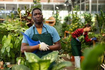 Man florist working in floral shop, watering flowers from a plastic watering can