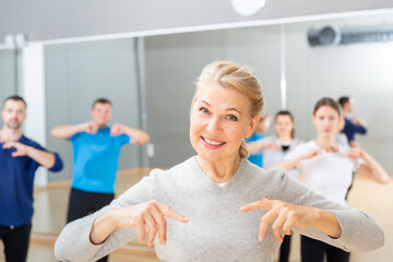 Portrait of sporty smiling mature woman practicing vigorous lindy hop movements in dance class