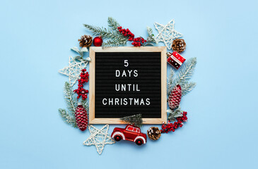 Felt letterboard with letters with countdown surrounded by winter seasonal decoration on blue background. 5 days until Christmas. Twenty-four day series of postcards. Selective focus