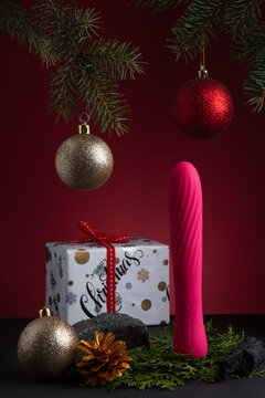 New Year or Christmas festive background for Sex shop. View on  pink dildo, red, silver and gold deco baubles, Christmas gift and tree. Image for the festive season and sales. Adult store. Sex toys.
