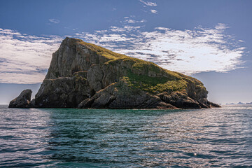 Resurrection Bay, Alaska, USA - July 22, 2011: Closeup of Hive Island shadow side, triangular rocky and partly covered by green vegetation under blue cloudscape