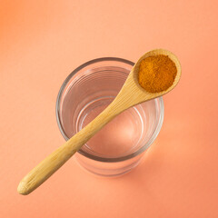 Spoon with organic turmeric and glass of filtered water - Curcuma longa