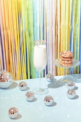 Milk in champagne glass with disco balls and chocolate cookies on a rainbow background. Christmas...