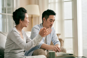 young asian adult son and elderly mother conversing at home