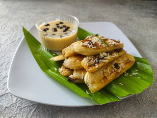 Grilled banana served with cheese sauce and chocolate chips on the white plate and placed on grey textured background. Selective focus image.
