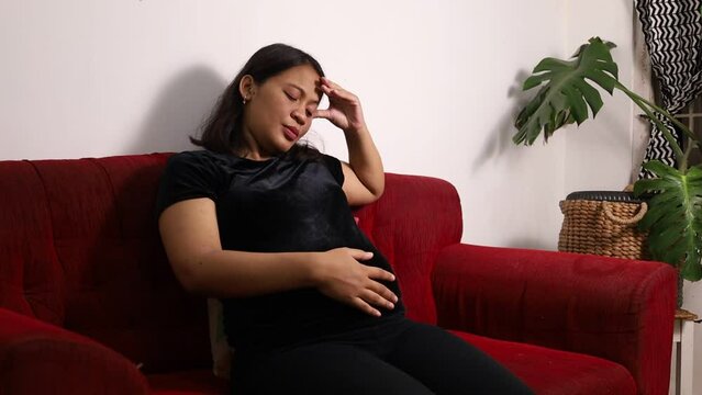 Asian Pregnant woman having headache while stroking the stomach at home