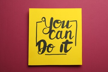 Yellow card with motivational phrase You Can Do It on burgundy background, top view
