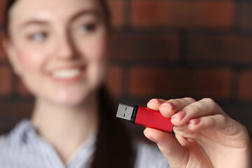 Woman holding usb flash drive near brick wall, focus on hand