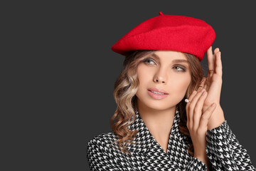 Young woman with beautiful makeup in red beret against black background. Space for text